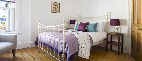 A bedroom with a metal bed frame, a bedside table with a lamp, and a window with a curtain.