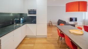 Eine moderne Küche mit weißen Schränken, einer schwarzen Arbeitsplatte und einem eingebauten Ofen. Ein Essbereich mit einem Holztisch und roten Stühlen ist ebenfalls vorhanden.