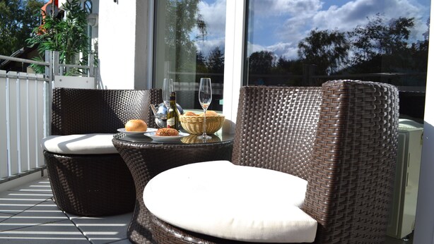 A balcony with wicker furniture, a glass table with a bottle and glasses, and a view of trees and sky. - KURPARK MAISONNETTE WILLINGEN ***** MOST REVIEWS - 2 BALCONIES - NL OWNER (Willingen (Upland))