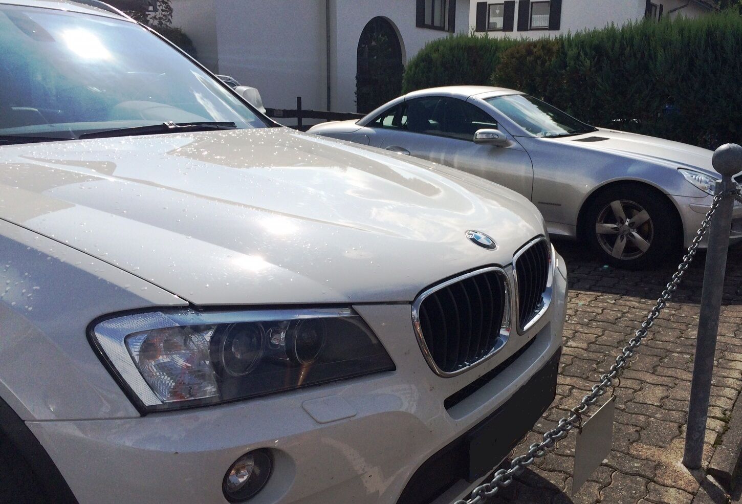 Een witte BMW geparkeerd op een geplaveid oppervlak, met een hekketting ervoor.