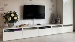 A modern living room with a flat-screen TV mounted on a white cabinet with floral wallpaper. - KURPARK MAISONNETTE WILLINGEN ***** MOST REVIEWS - 2 BALCONIES - NL OWNER (Willingen (Upland))