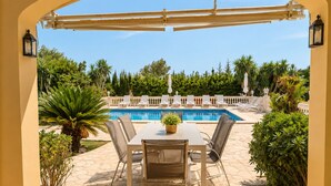 Eine Terrasse mit Tisch und Stühlen, ein Pool und Blick ins grüne Umland.