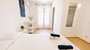 Ein Hotelzimmer mit einem großen Bett, einem kleinen Nachttisch, einem weißen Regal, einer Zimmerpflanze und einem Spiegel.