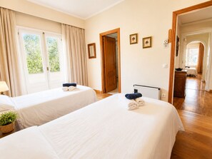 Habitació d'hotel amb dos llits, una finestra amb cortines, un radiador i una porta que condueix a una altra habitació.