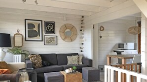 En moderne stue med en grå sofa, et træbord og et gråt tæppe. Væggen er udsmykket med indrammede kunstværker, et spejl og en hængende lampe.