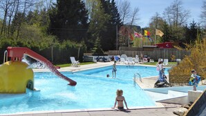En swimmingpool med rutsjebane, omgivet af liggestole og et træhegn.