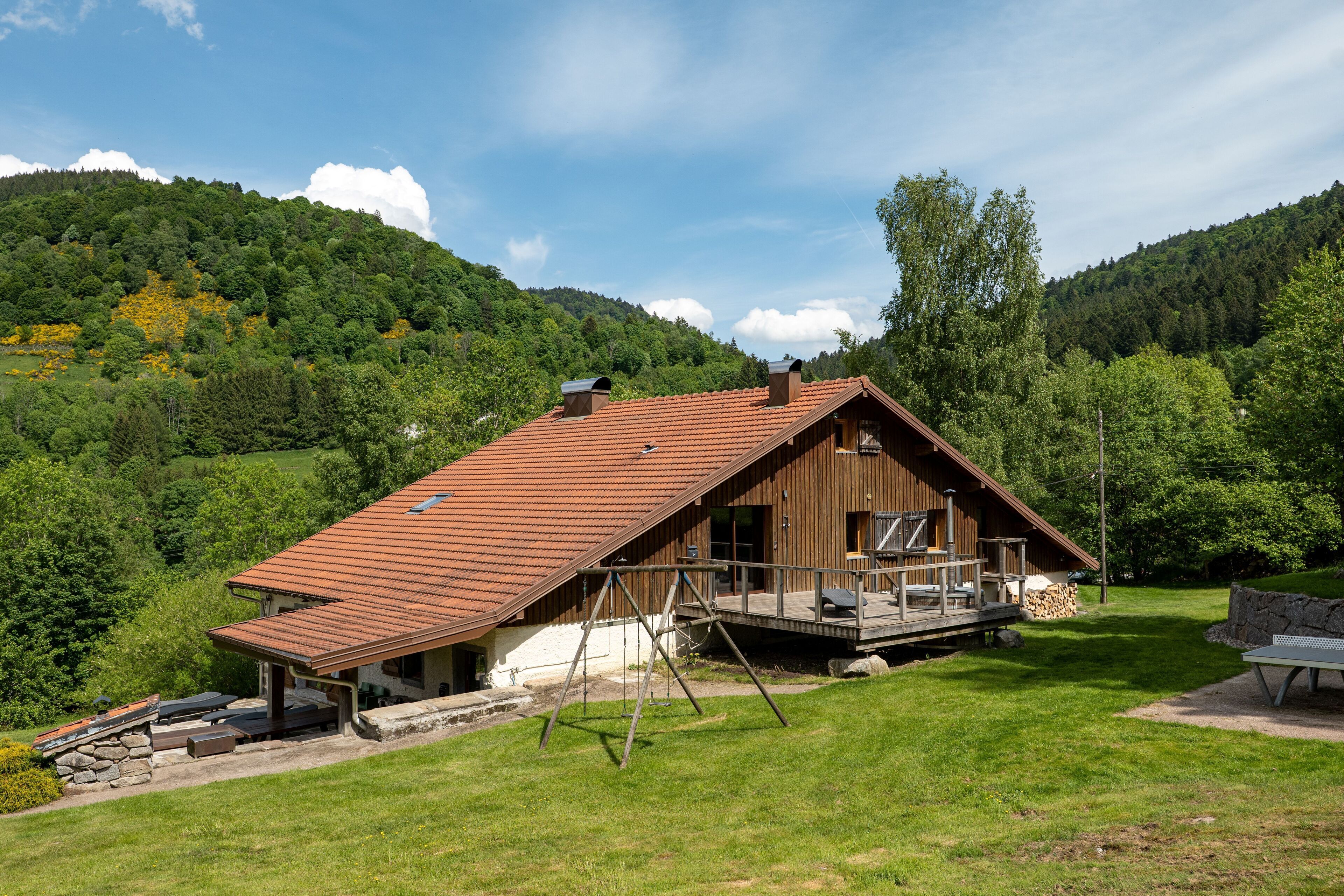 Une cabane en bois avec un toit en pente, une terrasse et un mur en pierre.