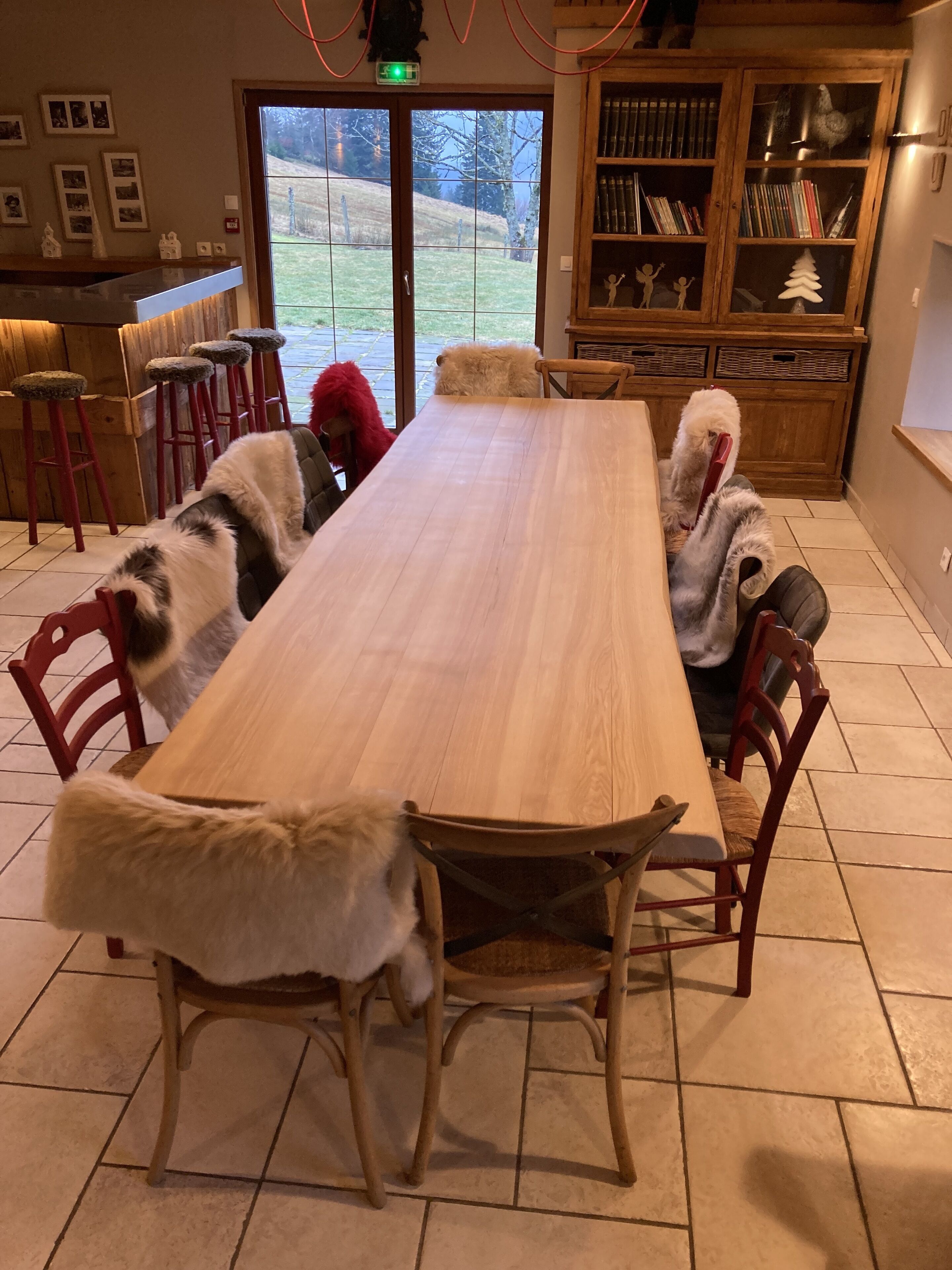Een eetgedeelte met een lange houten tafel, rode stoelen en een pluizige witte hond die op de vloer zit.