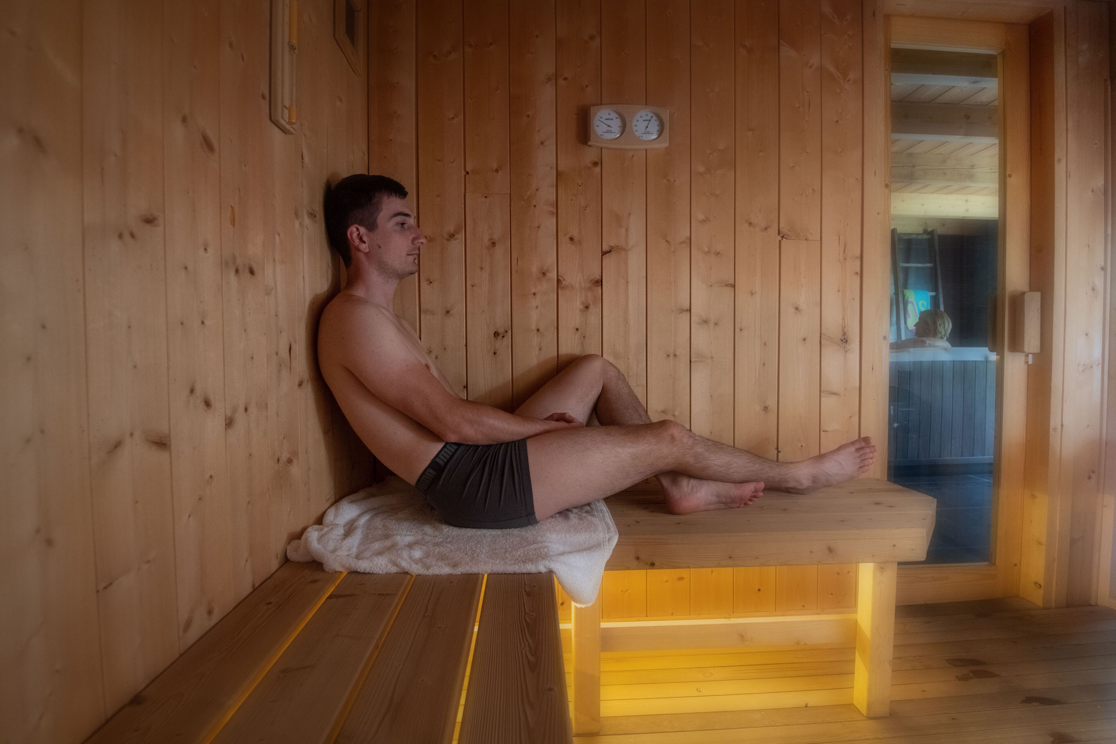 A wooden sauna with a bench, a clock, and a window.