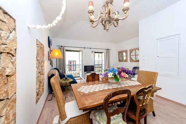 A dining area with a wooden table, wicker chairs, a chandelier, and a view through a glass door.