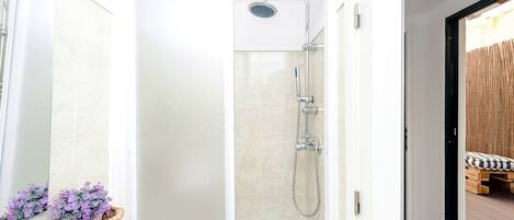 Un baño moderno con cabina de ducha de vidrio, un lavabo blanco y una planta decorativa.