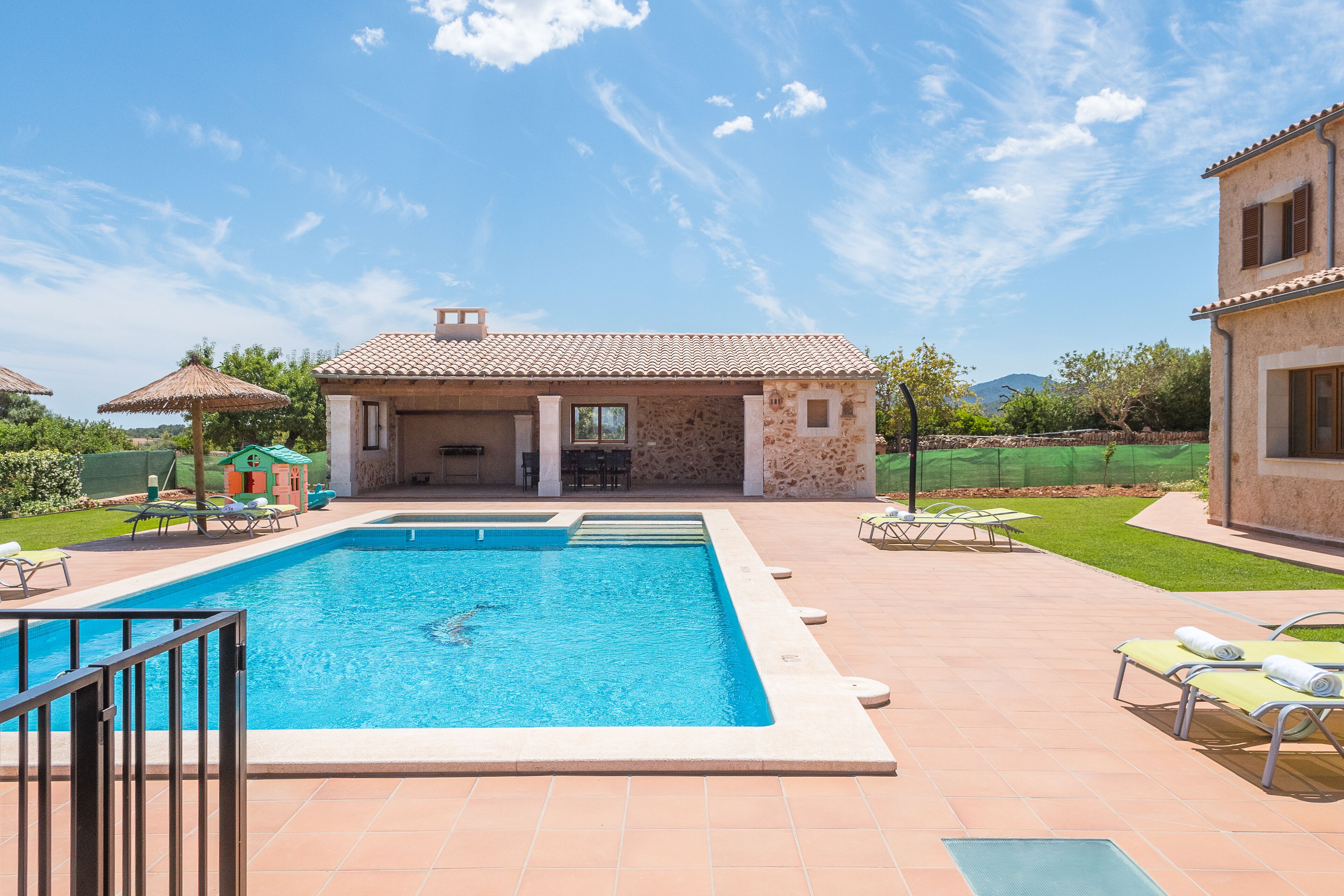 A swimming pool with lounge chairs, a covered patio, and a view of a mountain.