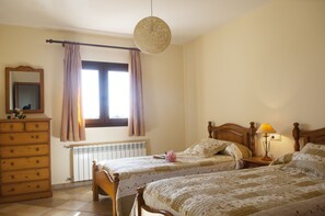 A bedroom with two beds, a dresser, a mirror, a window with curtains, a radiator, and a hanging light fixture. - DAYS OF REST AND RELAX IN THE COUNTRYSIDE AND NEAR THE BEACH (Manacor)
