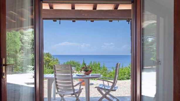 An open door leading to a patio with a table and two chairs, overlooking a scenic view of the sea. - Scrittore - SCRITTORE VILLA (Capoliveri)
