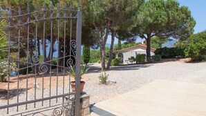 A gated property with a gravel driveway, trees, and a building with a red roof. - Scrittore - SCRITTORE VILLA (Capoliveri)