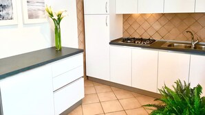 A modern kitchen with white cabinets, a black countertop, a gas stove, and a sink. There are framed pictures on the wall and a vase with flowers on the countertop. - Scrittore - SCRITTORE VILLA (Capoliveri)