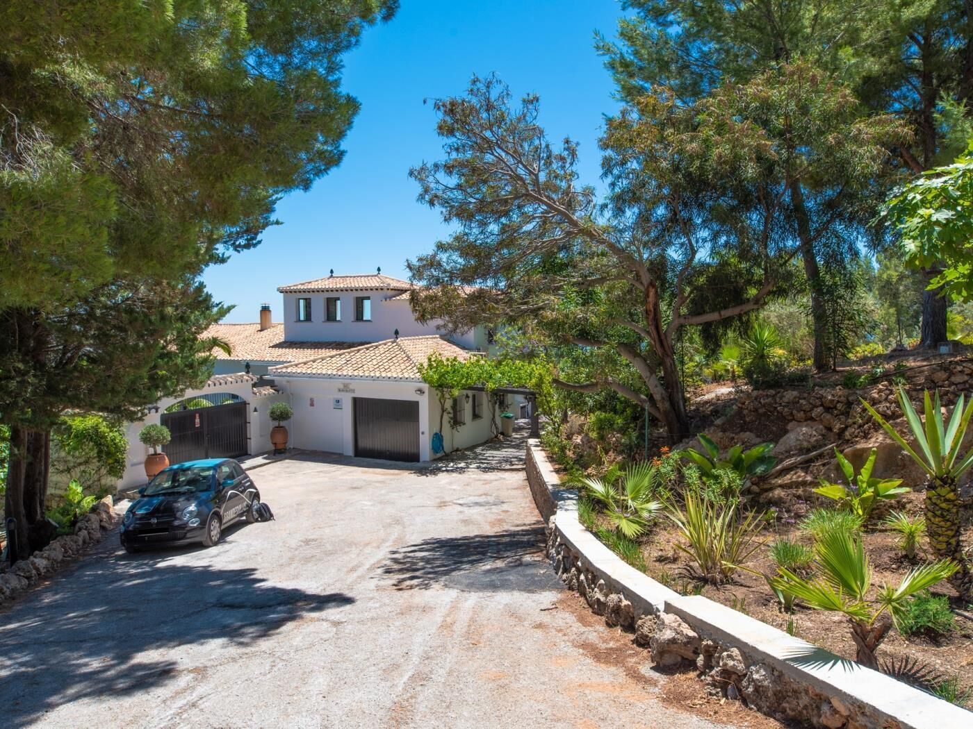A two-story house with a tiled roof, a garage, and a driveway leading to a parked car.