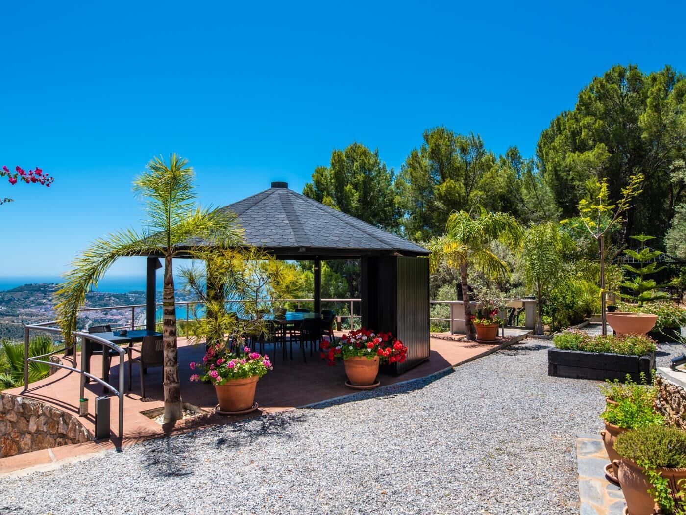 Un gazebo con un patio in ghiaia, circondato da piante in vaso e una vista panoramica.