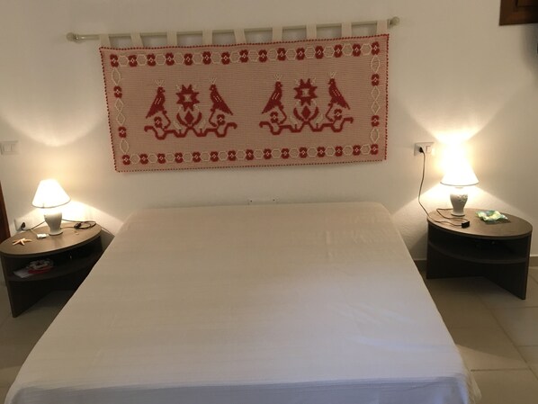 Ein Bett mit weißer Bettdecke, zwei Nachttische mit Lampen und ein dekoratives Wandbild darüber.