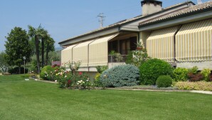 A house with a covered porch, a well-maintained lawn, and various plants and flowers. - APARTMENT INSIDE A VILLA, LARGE GARDEN WITH LAKE AND POOL VIEW (Bardolino)