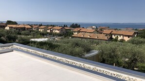 A coastal residential area with terracotta-roofed houses, a clear sky, and a view of the sea. - APARTMENT INSIDE A VILLA, LARGE GARDEN WITH LAKE AND POOL VIEW (Bardolino)