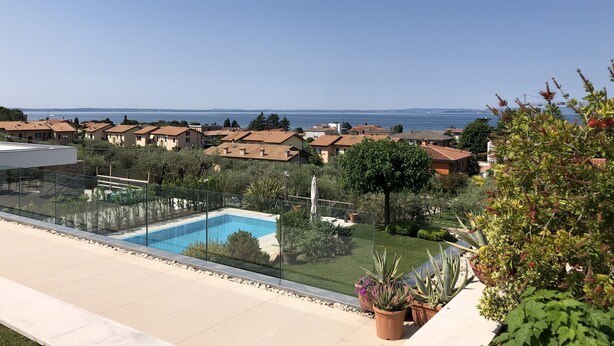 A residential area with a swimming pool, green lawns, and houses with red-tiled roofs. - APARTMENT INSIDE A VILLA, LARGE GARDEN WITH LAKE AND POOL VIEW (Bardolino)