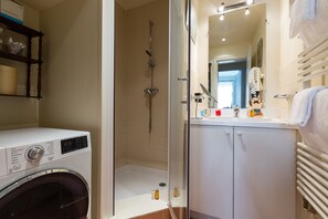 A modern bathroom with a glass-enclosed shower, a built-in washing machine, and a white vanity with a mirror.