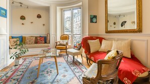 A cozy living room with a red sofa, a wooden chair, a glass coffee table, and a patterned rug.