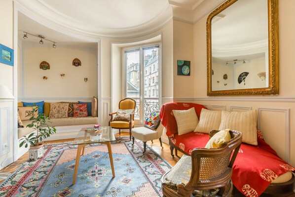 A cozy living room with a red sofa, a wooden chair, a glass coffee table, and a patterned rug.