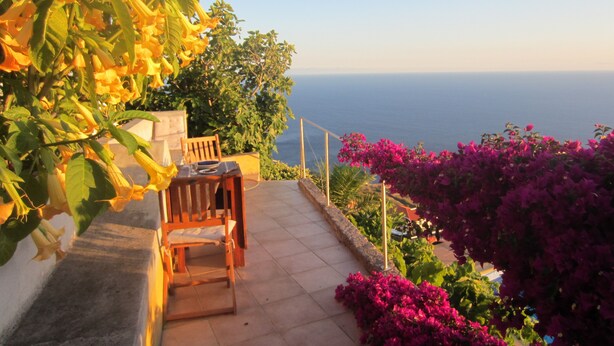 A terrace with a table and chair, overlooking the sea. - Villa with private pool, large garden and stunning sea view (Faja da Ovelha)