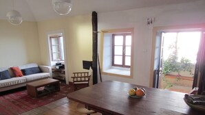 A living room with a sofa, coffee table, and a dining table with a fruit bowl. There is a window with a view of the outside. - Villa with private pool, large garden and stunning sea view (Faja da Ovelha)