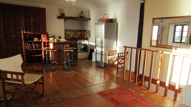 A spacious living area with a wooden floor, a dining table with chairs, a kitchen with a refrigerator, and a bookshelf.