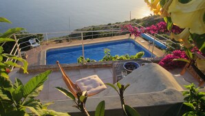 A swimming pool with a view of the sea, surrounded by greenery and flowers. - Villa with private pool, large garden and stunning sea view (Faja da Ovelha)