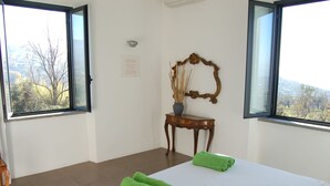 A hotel room with a large bed, two green towels, a wooden side table with a vase, and a mirror.