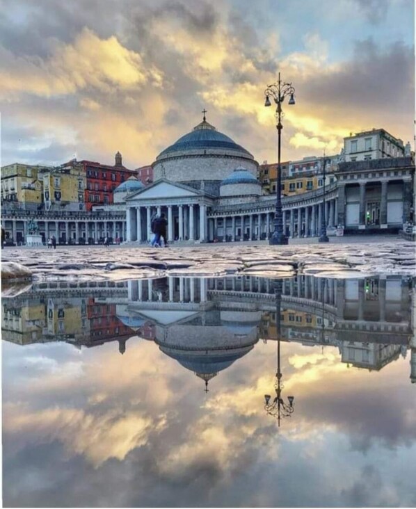 A historic building with a dome and classical architecture, reflected in a calm water surface.