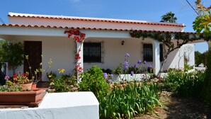 A white building with a tiled roof, a small porch, and a garden with various plants and flowers. - Villa with Private Swimming Pool / WI-Fi / Pet friendly (8700-176 Olhao)