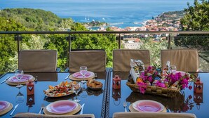 A table set for four with plates, cutlery, and glasses, overlooking a coastal town. - Artistsvillas-Red Rose,unique,with breathless sea views and ecological pool. (Gaios)