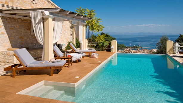 A poolside area with lounge chairs, a stone building, and a view of the sea. - Artistsvillas-Red Rose,unique,with breathless sea views and ecological pool. (Gaios)