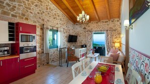 A kitchen with red cabinets, a dining area with a red tablecloth, and a stone wall. - Artistsvillas-Red Rose,unique,with breathless sea views and ecological pool. (Gaios)