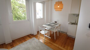 A compact kitchen with white cabinetry, a dining table with chairs, a hanging light fixture, and a window providing natural light. - OPO-APT 112-D Art Deco apartment in city center. AC, wi-fi, cozy and confortable (Portugal)
