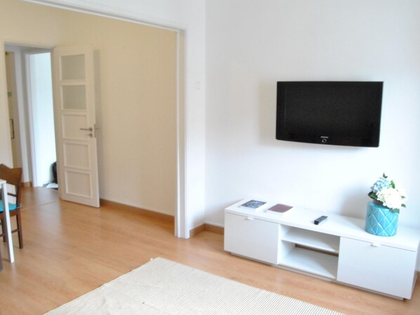 Un salon moderne avec un téléviseur à écran plat fixé au mur, un meuble de rangement blanc et un plancher en bois.