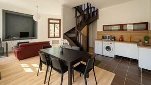Ein moderner Wohnraum mit Essbereich, einer Couch, einer Treppe, einer Küche und einem großen Fenster.