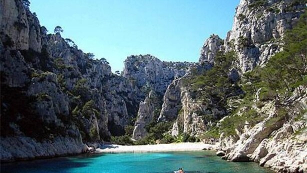 Eine Küstenlandschaft mit felsigen Klippen, klarem türkisblauem Wasser und einem Sandstrand.