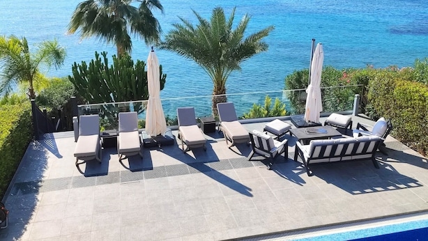 Un área junto a la piscina con sillones de descanso, sombrillas y vista al océano.
