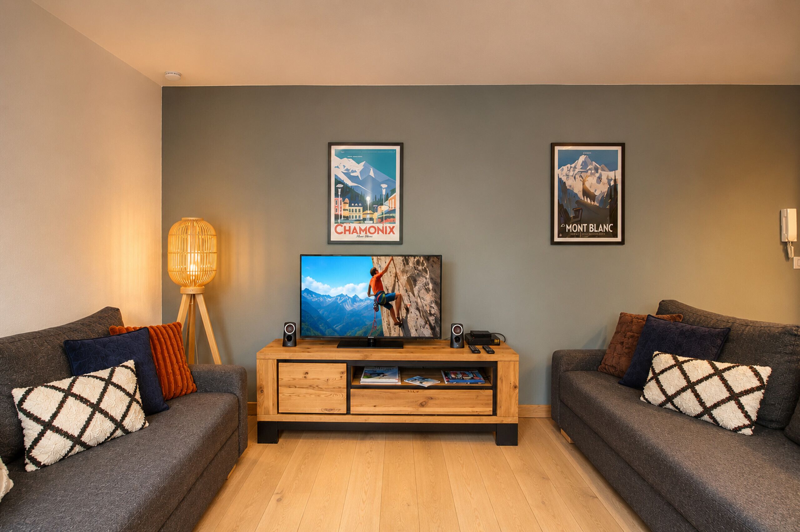 A living room with two sofas, a TV, framed posters, a lamp, and a wooden entertainment unit.