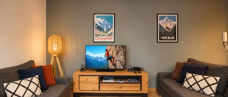 A living room with two sofas, a TV, framed posters, a lamp, and a wooden entertainment unit.