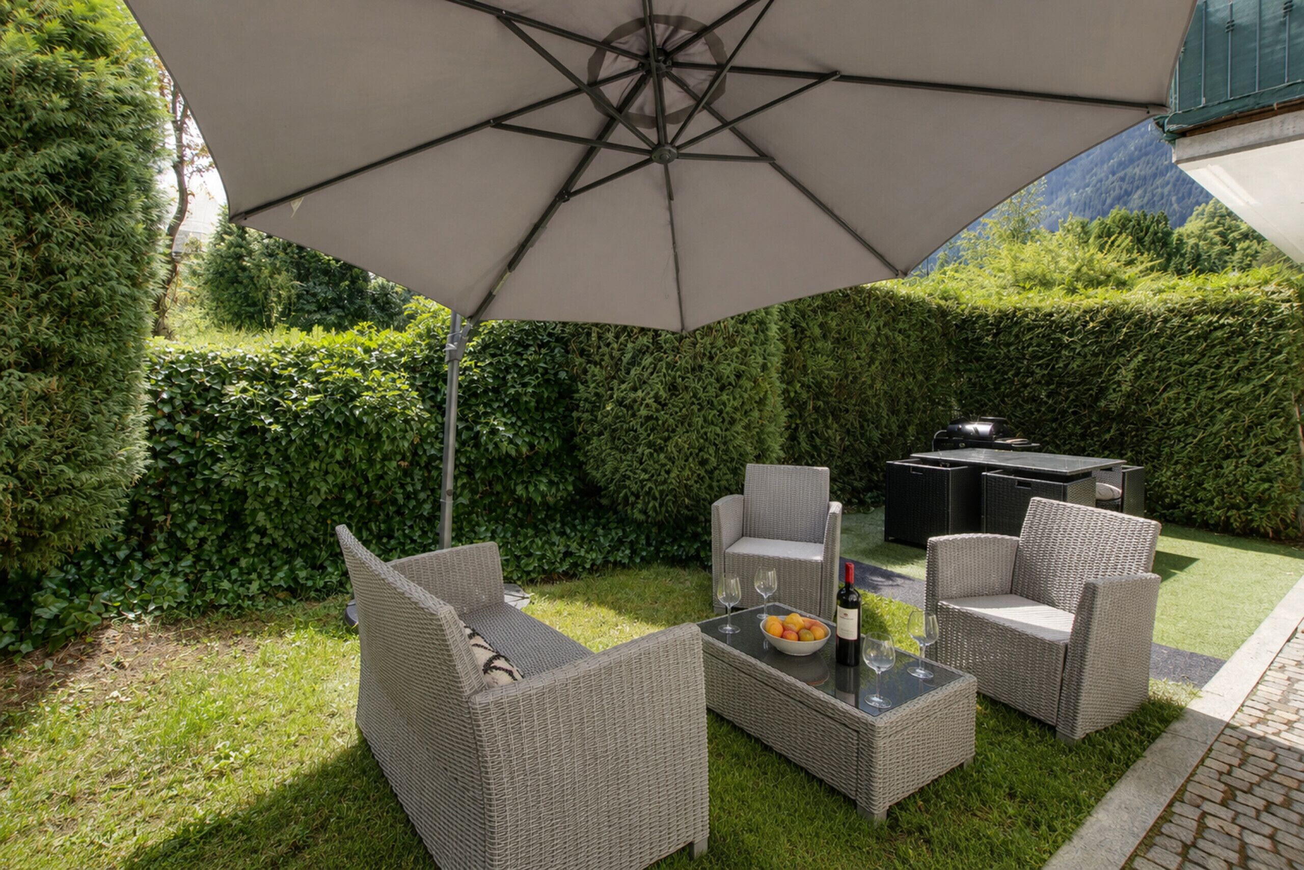 An outdoor patio area with wicker furniture, a table with a bottle and glasses, and a large umbrella.