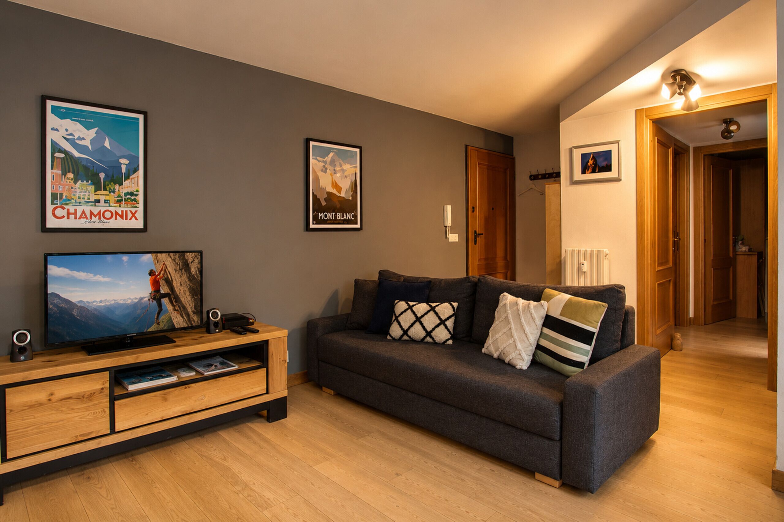 Een woonkamer met een grijze bank, een houten tv-meubel en twee ingelijste posters aan de muur.