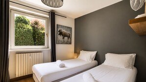 Ein Hotelzimmer mit zwei Betten, einem fenster mit Vorhängen, einem Heizkörper, einer Wandleuchte und einem Bild von einem Elch.