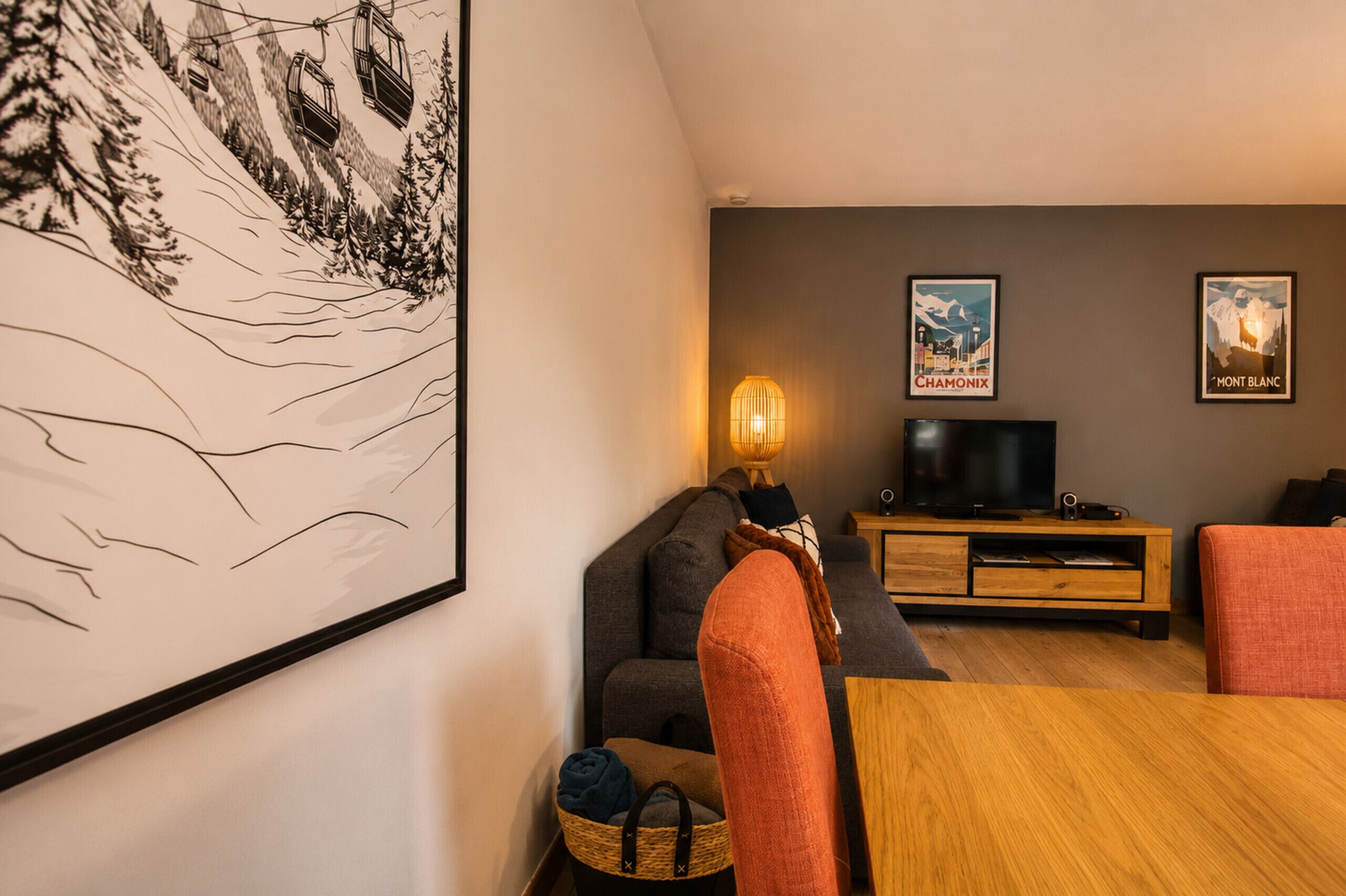Una sala de estar con un sofá, un televisor, una lámpara e imágenes enmarcadas en la pared.